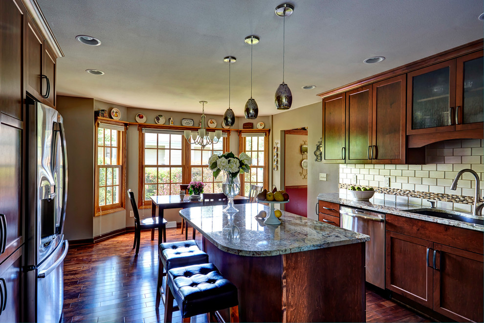 Large transitional l-shaped medium tone wood floor enclosed kitchen photo in Milwaukee with an undermount sink, shaker cabinets, medium tone wood cabinets, granite countertops, beige backsplash, glass tile backsplash, stainless steel appliances and an island