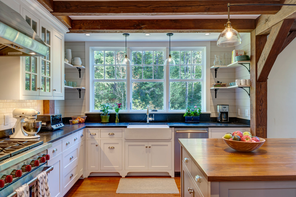 Photo of a mid-sized country l-shaped kitchen in Burlington with a farmhouse sink, white cabinets, soapstone benchtops, stainless steel appliances, medium hardwood floors, with island, shaker cabinets, white splashback and subway tile splashback.