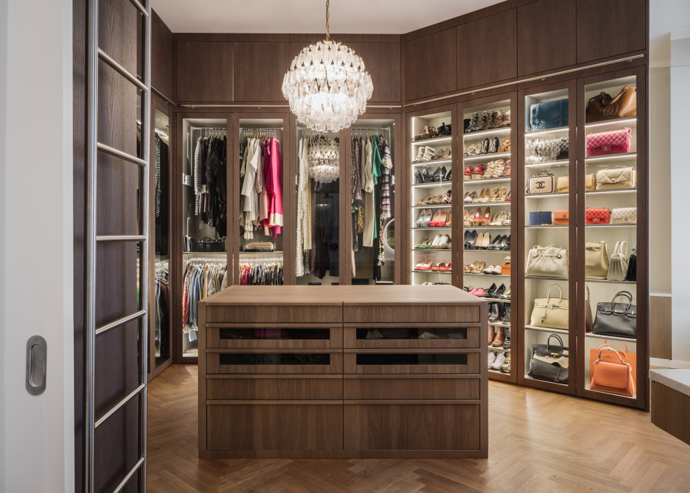 Inspiration for a large contemporary walk-in wardrobe for women in Berlin with glass-front cabinets, dark wood cabinets and light hardwood flooring.