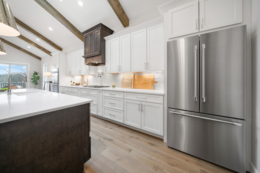 Transitional galley medium tone wood floor and vaulted ceiling open concept kitchen photo in Cincinnati with an undermount sink, shaker cabinets, white cabinets, quartz countertops, white backsplash, ceramic backsplash, stainless steel appliances, an island and white countertops
