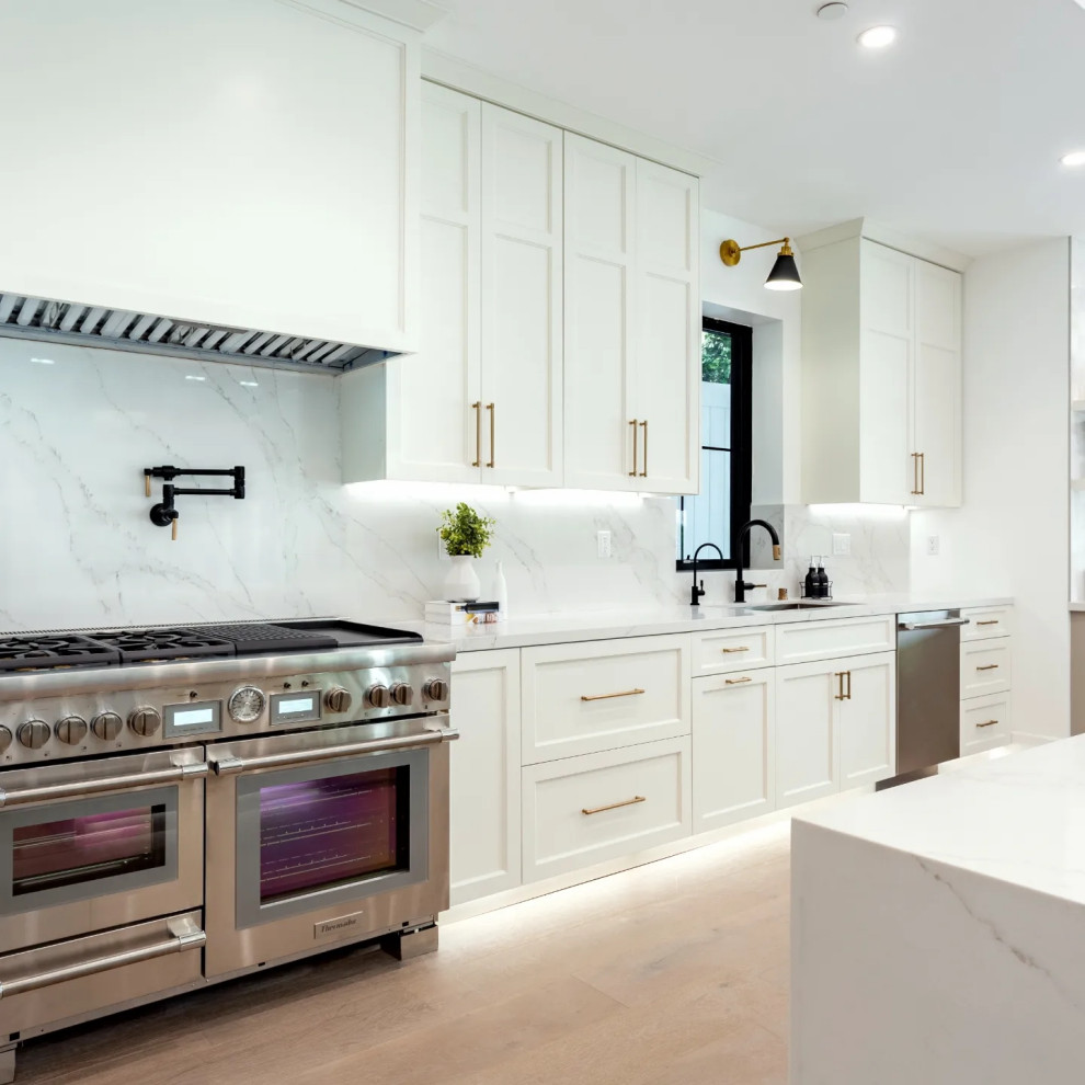 Inspiration for a large modern l-shaped open plan kitchen in Los Angeles with an undermount sink, shaker cabinets, white cabinets, quartz benchtops, white splashback, engineered quartz splashback, stainless steel appliances, medium hardwood floors, with island, beige floor and white benchtop.
