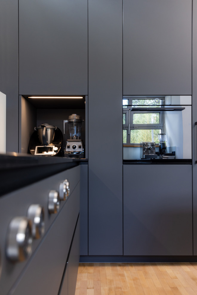 Kleine Moderne Küche in L-Form mit Vorratsschrank, offenen Schränken, grauen Schränken, Granit-Arbeitsplatte, schwarzen Elektrogeräten und schwarzer Arbeitsplatte in Frankfurt am Main
