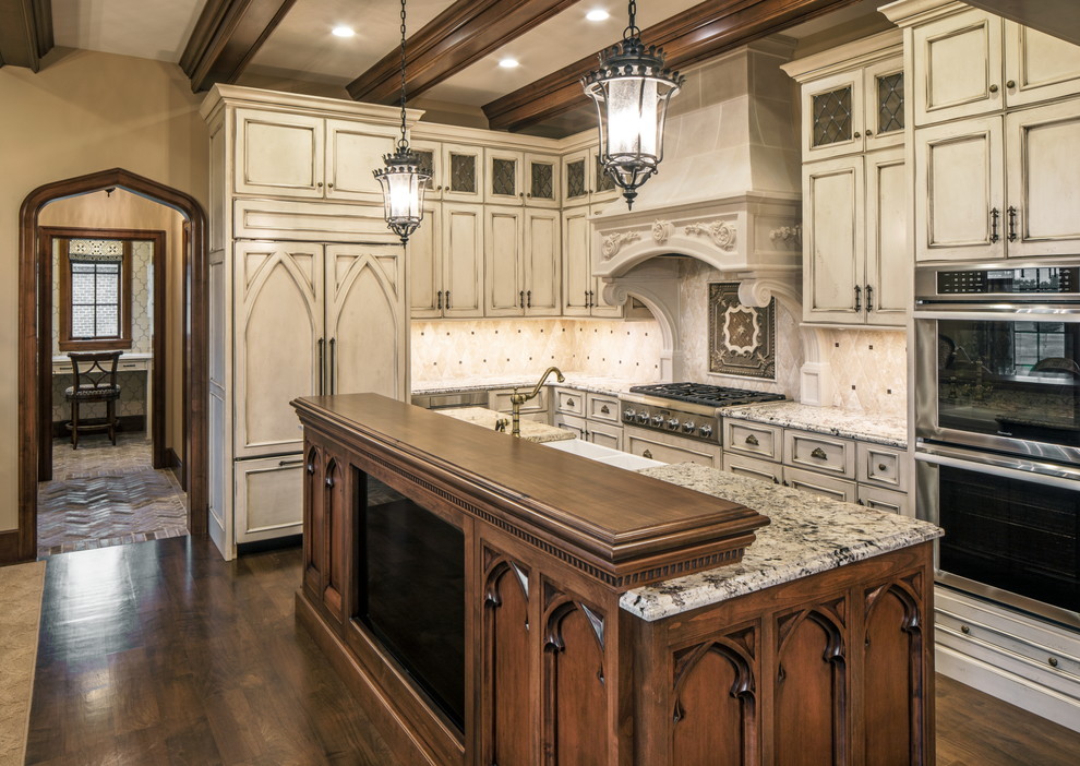 Traditional l-shaped kitchen in Omaha with a farmhouse sink, recessed-panel cabinets, beige cabinets, beige splashback, stainless steel appliances, dark hardwood floors, with island, brown floor and multi-coloured benchtop.