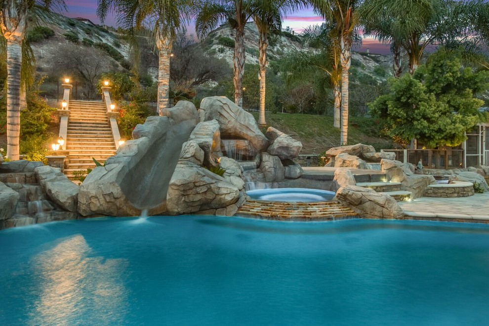 Inspiration for a large tropical backyard custom-shaped pool in Orange County with a water slide and concrete pavers.