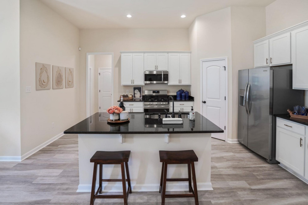 Medium sized classic kitchen in Other with white cabinets, granite worktops, stainless steel appliances, light hardwood flooring, an island, beige floors and black worktops.