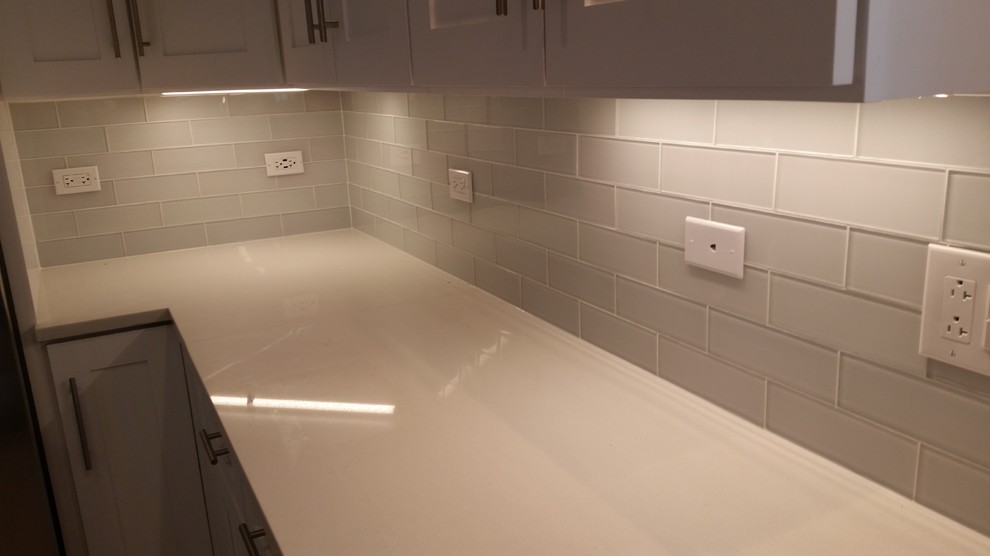 Example of a mid-sized minimalist galley dark wood floor eat-in kitchen design with an undermount sink, recessed-panel cabinets, white cabinets, granite countertops, white backsplash, glass tile backsplash, stainless steel appliances and a peninsula