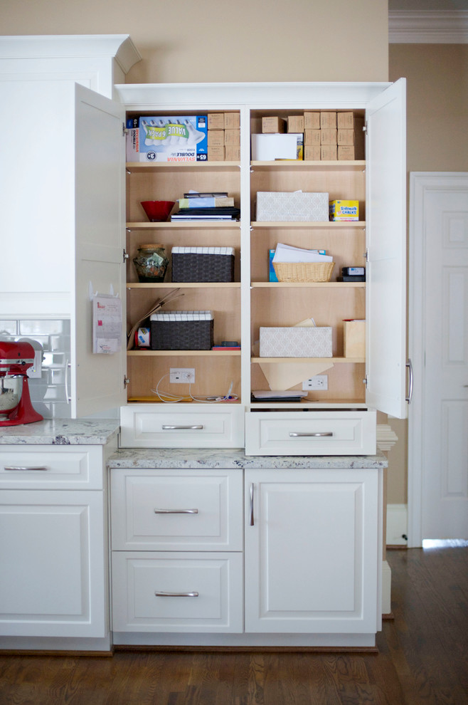 Open concept kitchen - mid-sized transitional l-shaped medium tone wood floor open concept kitchen idea in Atlanta with a farmhouse sink, raised-panel cabinets, white cabinets, granite countertops, gray backsplash, glass tile backsplash, stainless steel appliances and an island