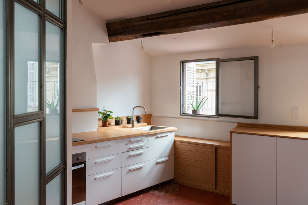 Small contemporary l-shaped open plan kitchen in Marseille with an undermount sink, beaded inset cabinets, white cabinets, wood benchtops, white splashback, ceramic splashback, stainless steel appliances, terra-cotta floors, no island and red floor.