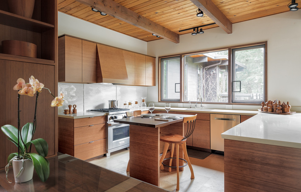 Inspiration for a midcentury u-shaped kitchen in Seattle with an undermount sink, flat-panel cabinets, medium wood cabinets, white splashback, glass sheet splashback, stainless steel appliances, with island, grey floor and white benchtop.