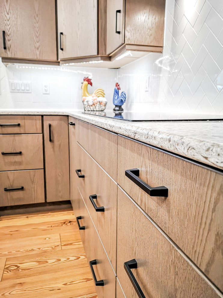 Example of a large u-shaped light wood floor and brown floor eat-in kitchen design with an undermount sink, flat-panel cabinets, beige cabinets, quartz countertops, white backsplash, subway tile backsplash, stainless steel appliances, an island and white countertops