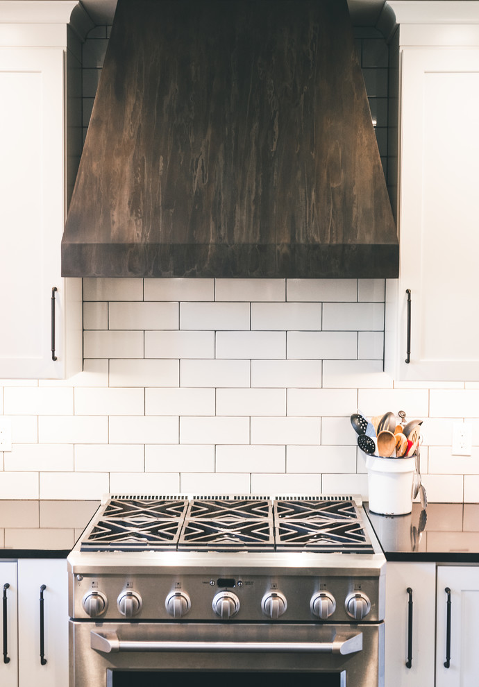 Inspiration for a large country u-shaped kitchen in Seattle with a farmhouse sink, shaker cabinets, white cabinets, quartz benchtops, white splashback, subway tile splashback, stainless steel appliances, black floor and black benchtop.
