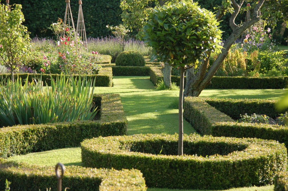 Cette image montre un grand jardin à la française arrière traditionnel l'été avec une exposition partiellement ombragée et du gravier.
