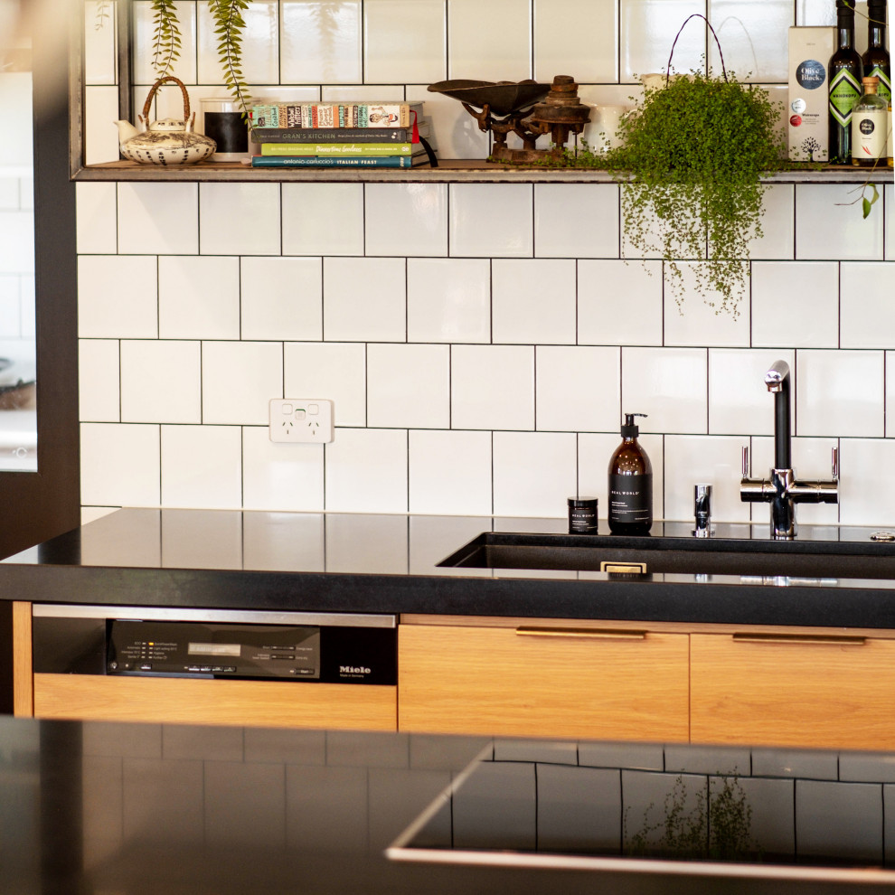 Photo of a large contemporary galley eat-in kitchen in Auckland with a drop-in sink, medium wood cabinets, granite benchtops, white splashback, subway tile splashback, stainless steel appliances, medium hardwood floors, with island, brown floor and black benchtop.