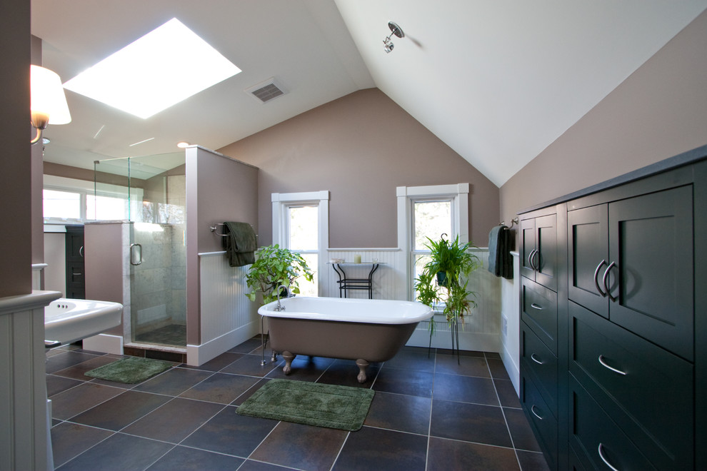 This is an example of a mid-sized traditional master bathroom in Detroit with shaker cabinets, black cabinets, a freestanding tub, an alcove shower, a two-piece toilet, beige tile, limestone, multi-coloured walls, ceramic floors, a pedestal sink, brown floor and a hinged shower door.