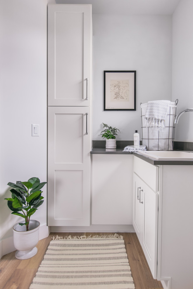 Design ideas for a mid-sized arts and crafts u-shaped dedicated laundry room in Tampa with an utility sink, shaker cabinets, white cabinets, quartz benchtops, white walls, light hardwood floors, a side-by-side washer and dryer, beige floor and grey benchtop.