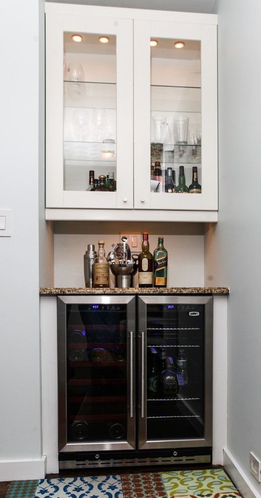 Photo of a small contemporary u-shaped wet bar in New York with no sink, shaker cabinets, white cabinets, solid surface benchtops, black splashback and medium hardwood floors.
