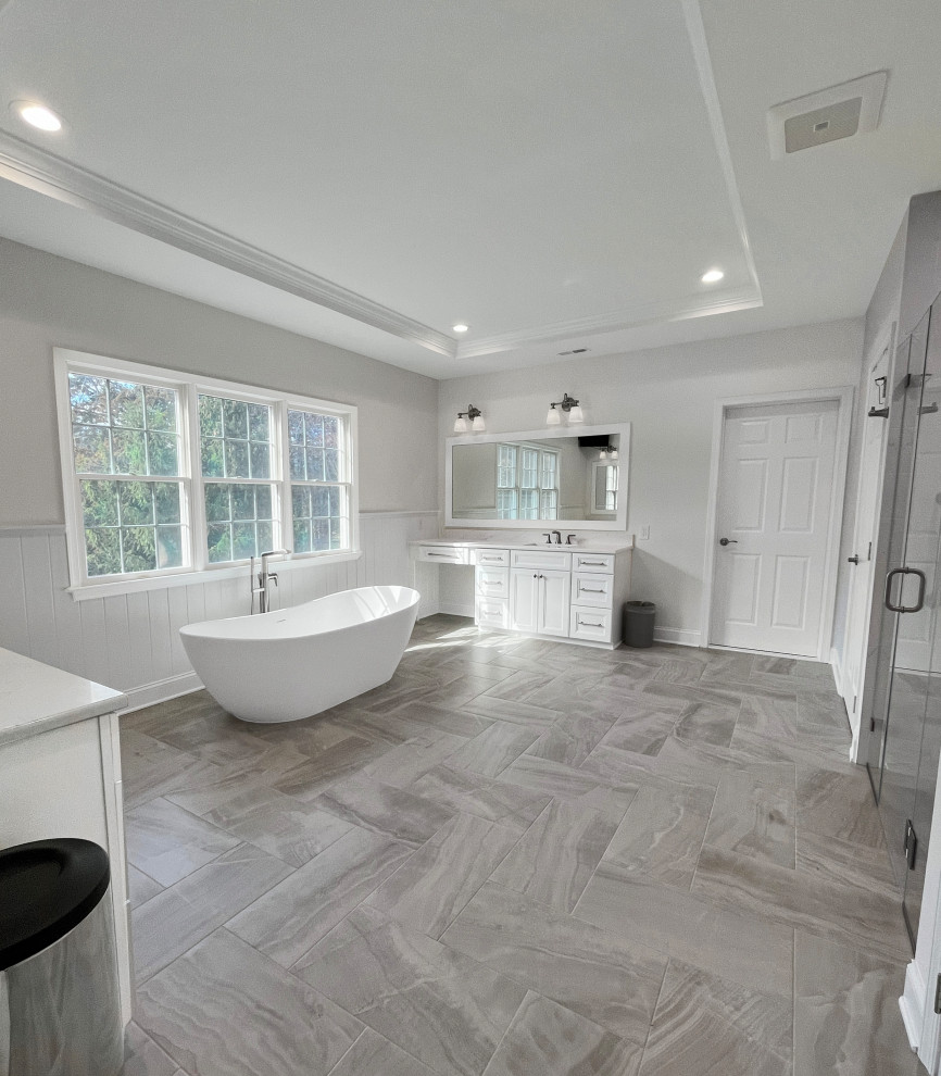 Photo of a large traditional ensuite bathroom in Philadelphia with recessed-panel cabinets, white cabinets, a freestanding bath, a double shower, a one-piece toilet, grey tiles, ceramic tiles, grey walls, porcelain flooring, a submerged sink, engineered stone worktops, grey floors, a hinged door, white worktops, a wall niche, double sinks, a built in vanity unit, a drop ceiling and wainscoting.
