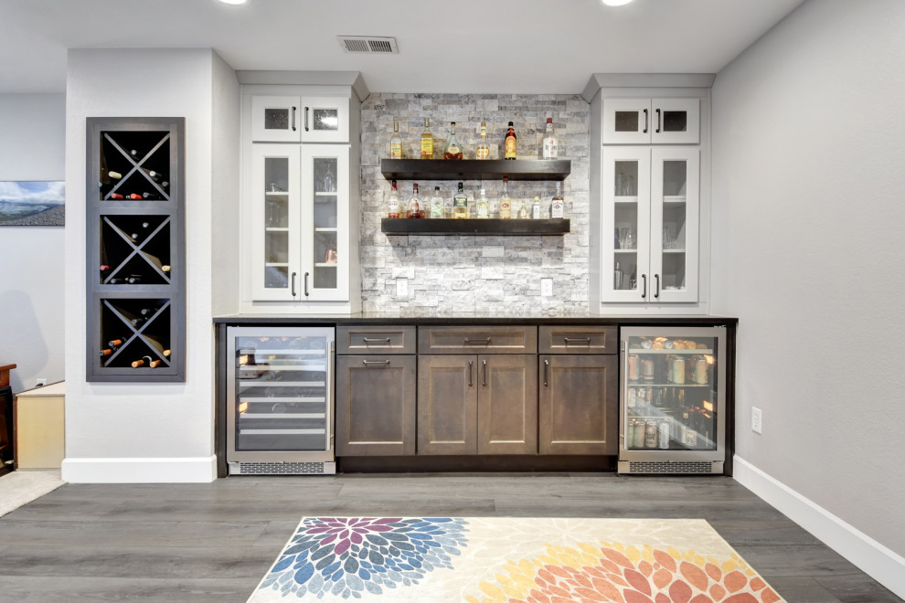 This is an example of a rural single-wall wet bar in Denver with no sink, glass-front cabinets, white cabinets, quartz worktops, white splashback, stone tiled splashback, laminate floors, grey floors and black worktops.