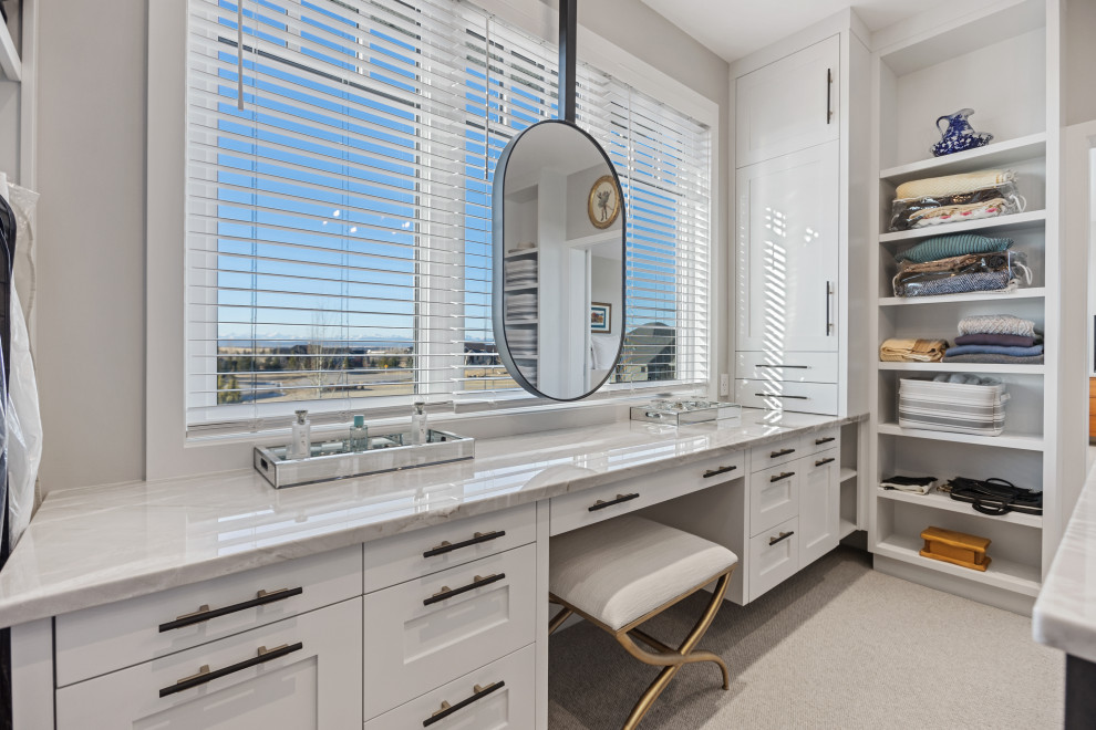 Réalisation d'un grand dressing design neutre avec un placard à porte shaker, des portes de placard blanches, moquette et un sol beige.