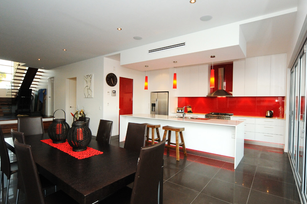 This is an example of a contemporary galley open plan kitchen in Brisbane with a double-bowl sink, flat-panel cabinets, white cabinets, red splashback, glass sheet splashback and stainless steel appliances.