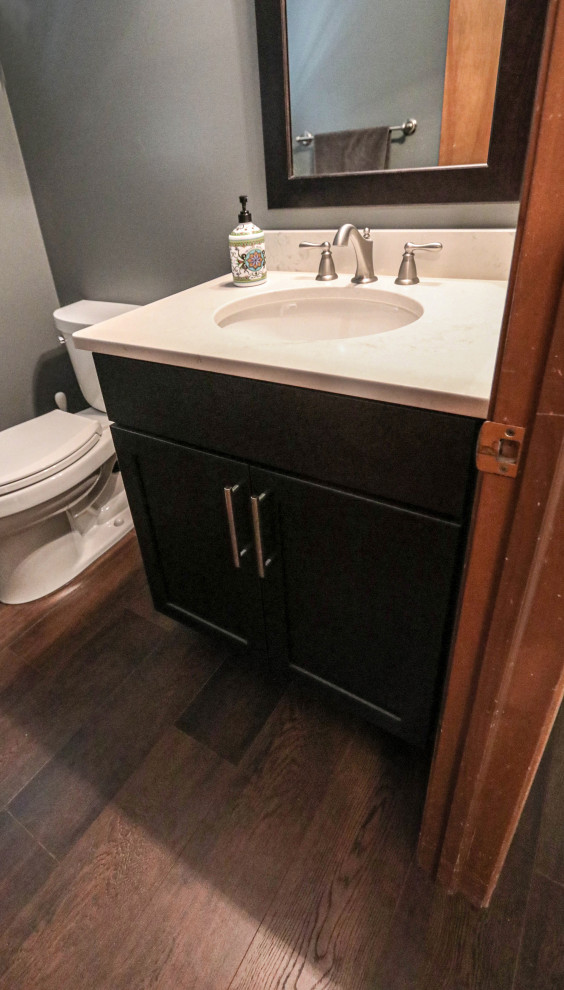 Cette image montre un petit WC et toilettes traditionnel avec un placard à porte plane, des portes de placard noires, WC séparés, un sol en vinyl, un lavabo encastré, un plan de toilette en quartz modifié, un sol marron, un plan de toilette blanc et meuble-lavabo sur pied.