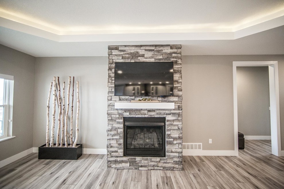 Photo of a mid-sized transitional open concept family room in Cedar Rapids with grey walls, laminate floors, a standard fireplace, a stone fireplace surround, a wall-mounted tv and brown floor.