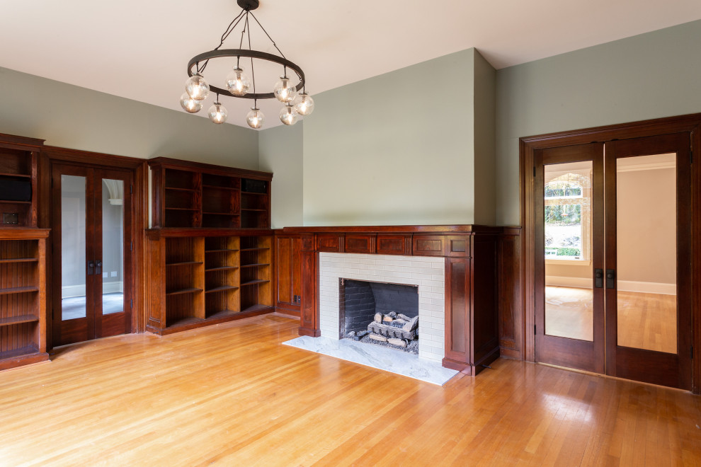 Photo of a mid-sized traditional home office in Portland with a library, green walls, light hardwood floors, a standard fireplace, a brick fireplace surround, brown floor and wood walls.