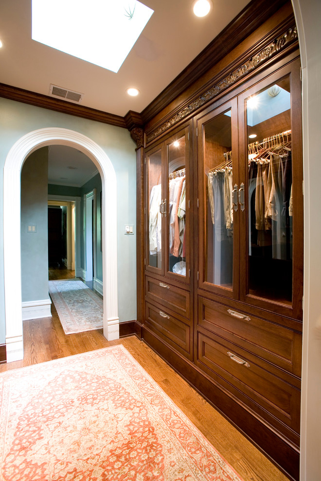 This is an example of a traditional built-in wardrobe in Chicago with glass-front cabinets and dark wood cabinets.