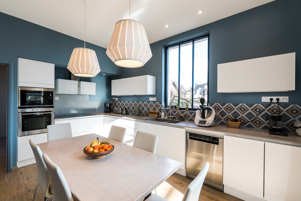Mid-sized contemporary l-shaped eat-in kitchen in Lyon with flat-panel cabinets, white cabinets, stainless steel benchtops, multi-coloured splashback, ceramic splashback, medium hardwood floors, no island, a double-bowl sink and stainless steel appliances.