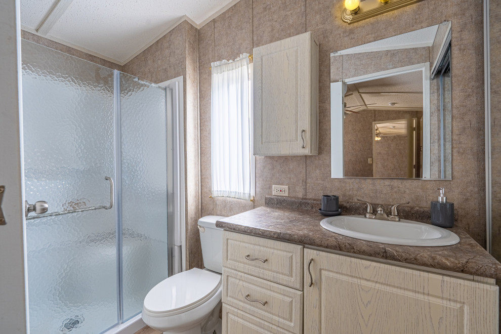This is an example of a small farmhouse shower room bathroom in Other with raised-panel cabinets, a built in vanity unit, white cabinets, an alcove shower, a one-piece toilet, beige walls, lino flooring, a built-in sink, brown floors, a hinged door, beige worktops, a laundry area, a single sink, exposed beams and panelled walls.
