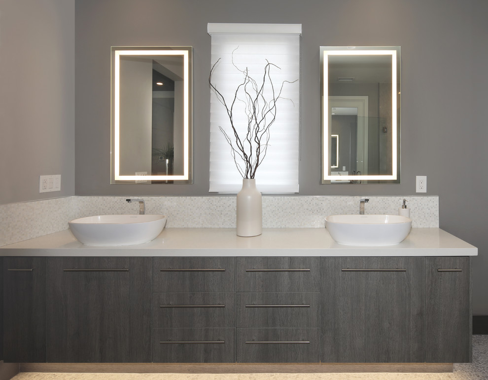 Design ideas for a mid-sized modern master bathroom with flat-panel cabinets, dark wood cabinets, a freestanding tub, a corner shower, gray tile, stone slab, grey walls, pebble tile floors, a vessel sink, engineered quartz benchtops, a hinged shower door and white benchtops.