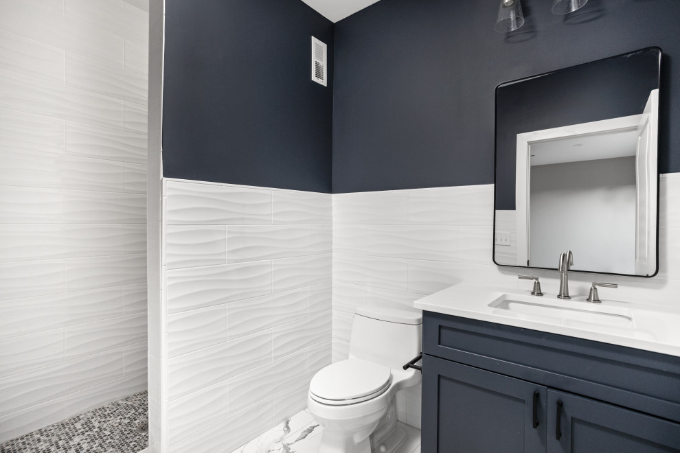 На фото: детская ванная комната среднего размера в стиле неоклассика (современная классика) с фасадами в стиле шейкер, синими фасадами, душем в нише, унитазом-моноблоком, белой плиткой, керамической плиткой, синими стенами, полом из керамической плитки, врезной раковиной, столешницей из искусственного кварца, белым полом, душем с распашными дверями, белой столешницей, нишей, тумбой под одну раковину и встроенной тумбой с