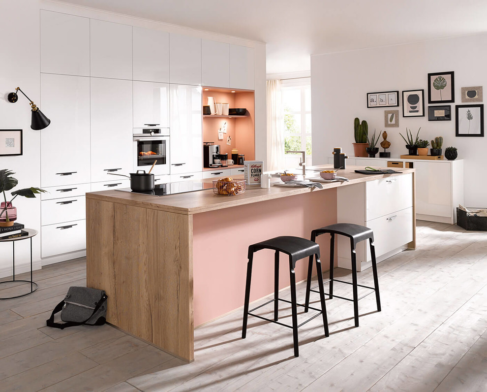 Large modern single-wall open plan kitchen in Surrey with an undermount sink, flat-panel cabinets, white cabinets, wood benchtops, pink splashback, white appliances, light hardwood floors, with island and grey floor.