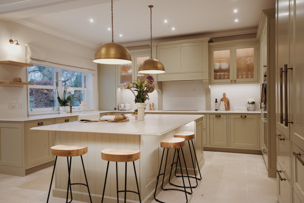 This is an example of a large traditional u-shaped eat-in kitchen in London with an undermount sink, shaker cabinets, green cabinets, quartzite benchtops, white splashback, subway tile splashback, panelled appliances, limestone floors, with island, white floor and white benchtop.