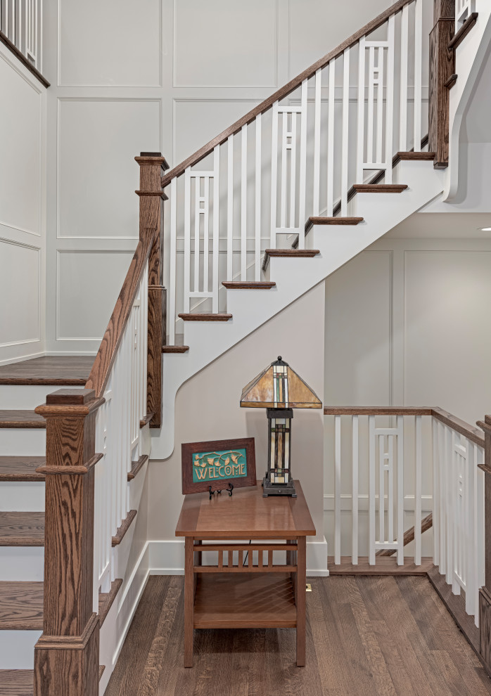 На фото: большая п-образная лестница в стиле кантри с деревянными ступенями, крашенными деревянными подступенками, деревянными перилами и панелями на части стены с