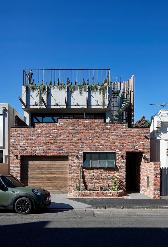 Réalisation d'une façade de maison rouge urbaine en brique de taille moyenne et à un étage avec un toit plat.