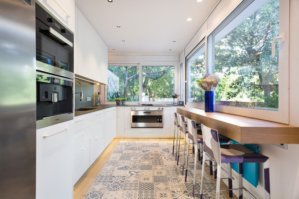 Large contemporary l-shaped open plan kitchen in Barcelona with flat-panel cabinets, white cabinets, stainless steel appliances, ceramic floors, no island, multi-coloured floor, an integrated sink, quartz benchtops and black splashback.