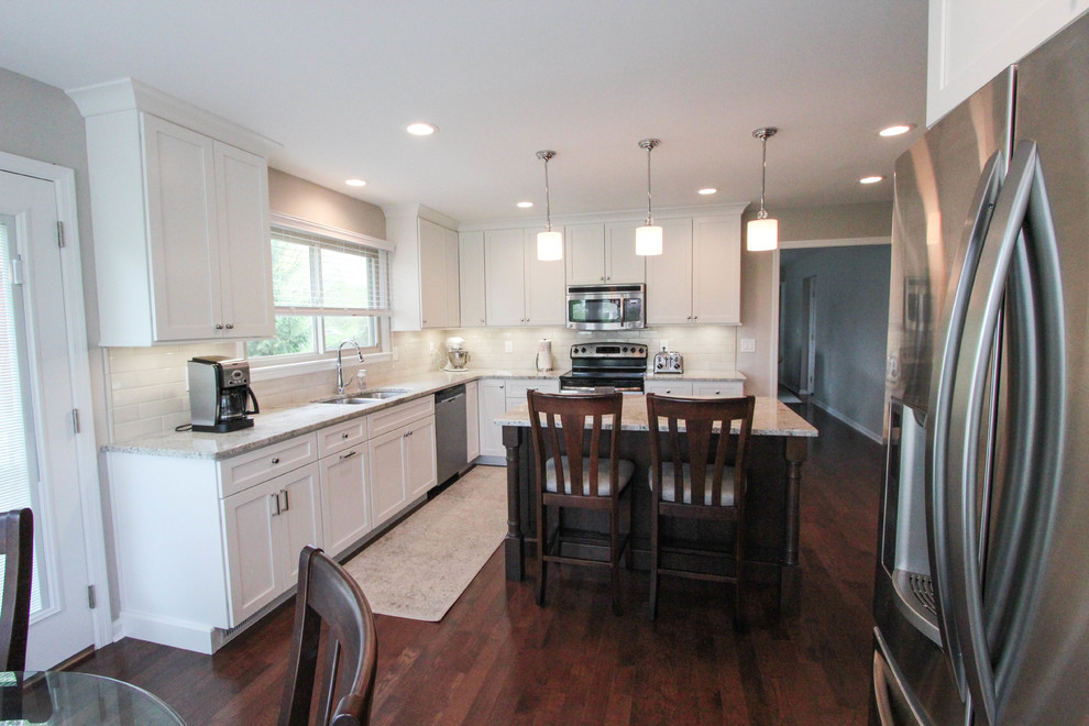 Enclosed kitchen - mid-sized transitional l-shaped dark wood floor and brown floor enclosed kitchen idea in Cincinnati with an undermount sink, shaker cabinets, white cabinets, granite countertops, beige backsplash, porcelain backsplash, stainless steel appliances, an island and white countertops