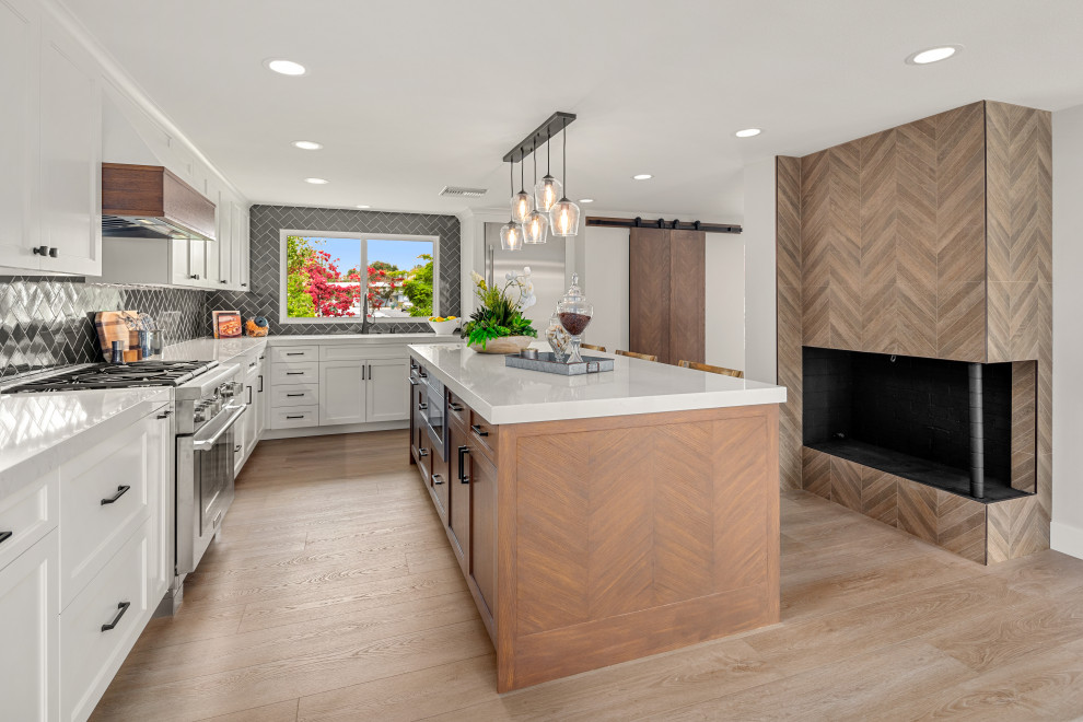 Example of a mid-sized country l-shaped laminate floor eat-in kitchen design in Orange County with a farmhouse sink, shaker cabinets, white cabinets, quartz countertops, blue backsplash, ceramic backsplash, stainless steel appliances and an island