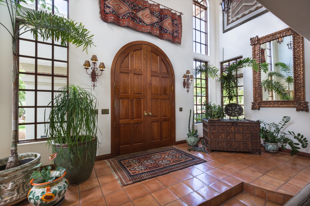 Photo of a mid-sized mediterranean foyer in Las Vegas with white walls, terra-cotta floors, a double front door and a dark wood front door.