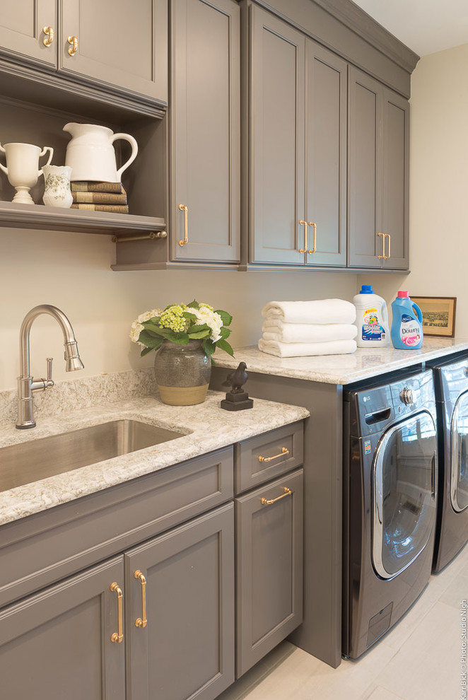 This is an example of a small transitional single-wall dedicated laundry room in St Louis with an undermount sink, grey cabinets, quartz benchtops, beige walls, porcelain floors, a side-by-side washer and dryer, white floor and recessed-panel cabinets.