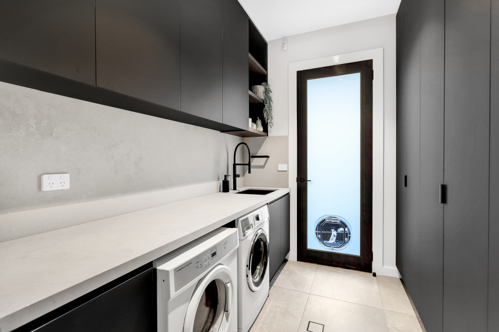 This is an example of a mid-sized contemporary galley laundry room in Sydney with a drop-in sink, black cabinets, quartzite benchtops, white walls, porcelain floors, a side-by-side washer and dryer and white floor.