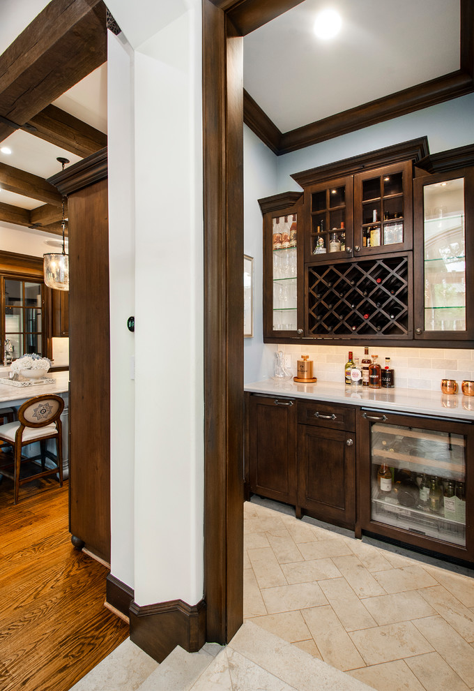Photo of a mid-sized traditional single-wall home bar in Dallas with no sink, recessed-panel cabinets, dark wood cabinets, white splashback, porcelain floors, beige floor and white benchtop.