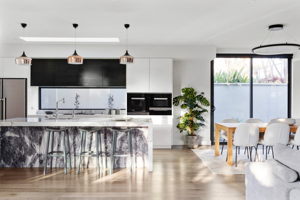 This is an example of a large modern galley eat-in kitchen in Melbourne with an undermount sink, black cabinets, marble benchtops, stainless steel appliances, light hardwood floors, with island, beige floor and white benchtop.