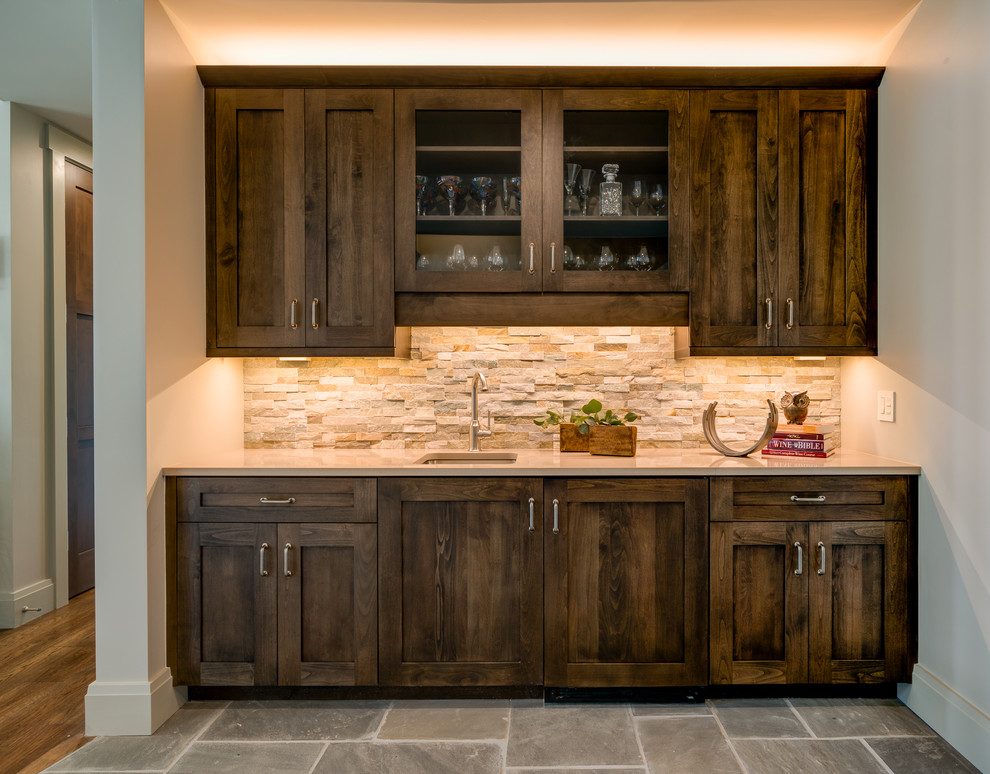 This is an example of a large country single-wall wet bar in Other with an undermount sink, shaker cabinets, quartz benchtops, beige splashback, stone tile splashback, dark wood cabinets and grey floor.