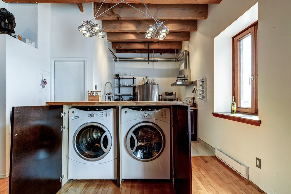 Inspiration for a small industrial laundry cupboard in Montreal with a side-by-side washer and dryer, flat-panel cabinets, medium wood cabinets, wood benchtops, white walls and medium hardwood floors.