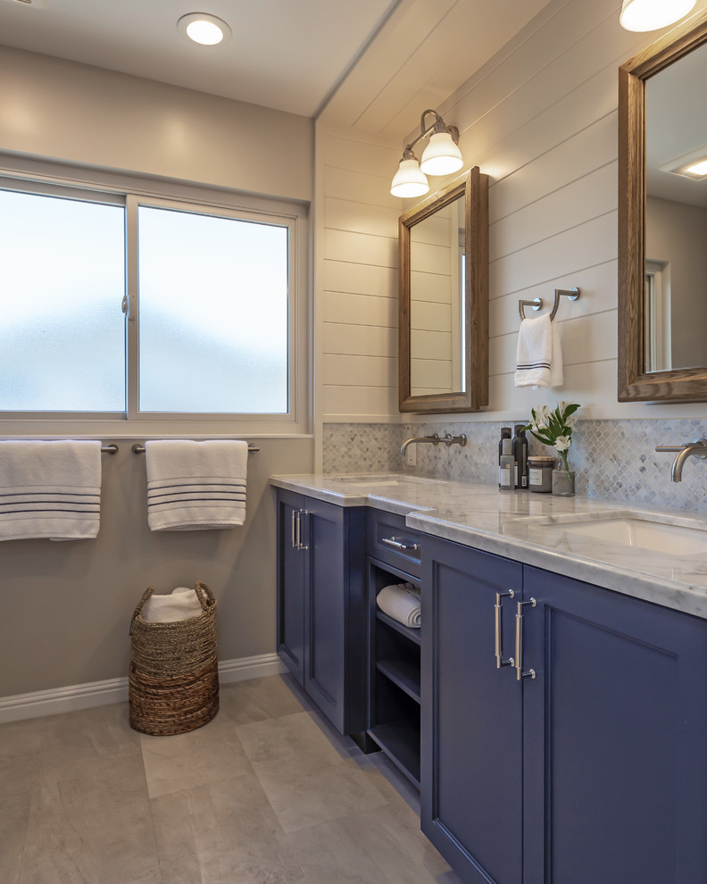 Photo of a mid-sized transitional kids bathroom in San Francisco with shaker cabinets, blue cabinets, an undermount tub, a shower/bathtub combo, a one-piece toilet, gray tile, marble, grey walls, vinyl floors, an undermount sink, engineered quartz benchtops, grey floor, a shower curtain and white benchtops.