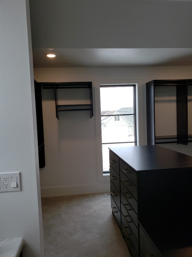 This is an example of a transitional gender-neutral walk-in wardrobe in Other with flat-panel cabinets, black cabinets, carpet and beige floor.