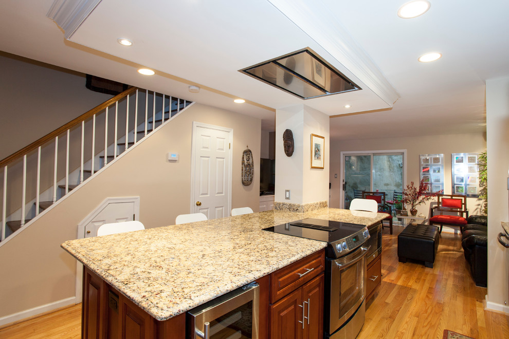 Mid-sized transitional galley open plan kitchen in Philadelphia with an undermount sink, raised-panel cabinets, dark wood cabinets, granite benchtops, white splashback, subway tile splashback, stainless steel appliances, light hardwood floors and with island.