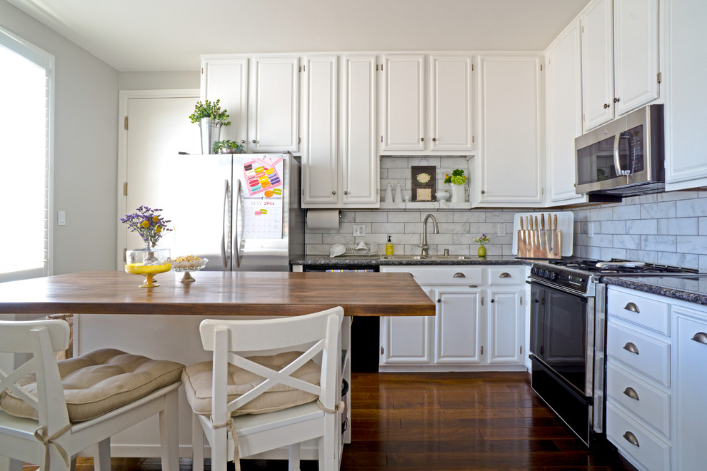 This is an example of a mid-sized transitional l-shaped kitchen in San Francisco with a drop-in sink, raised-panel cabinets, white cabinets, white splashback, stainless steel appliances, dark hardwood floors, with island and marble splashback.